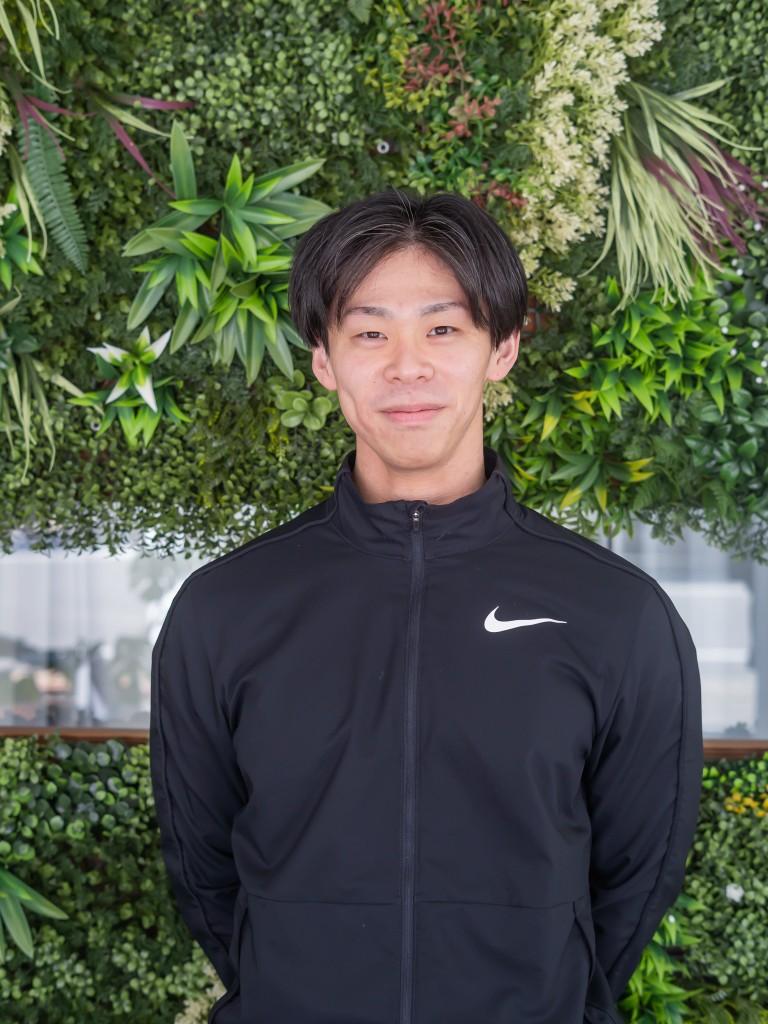 渡邉 亮太。グリーンウォールの前で微笑むポートレート。